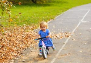 Kleines Mädchen auf einem Laufrad im Herbst unterwegs